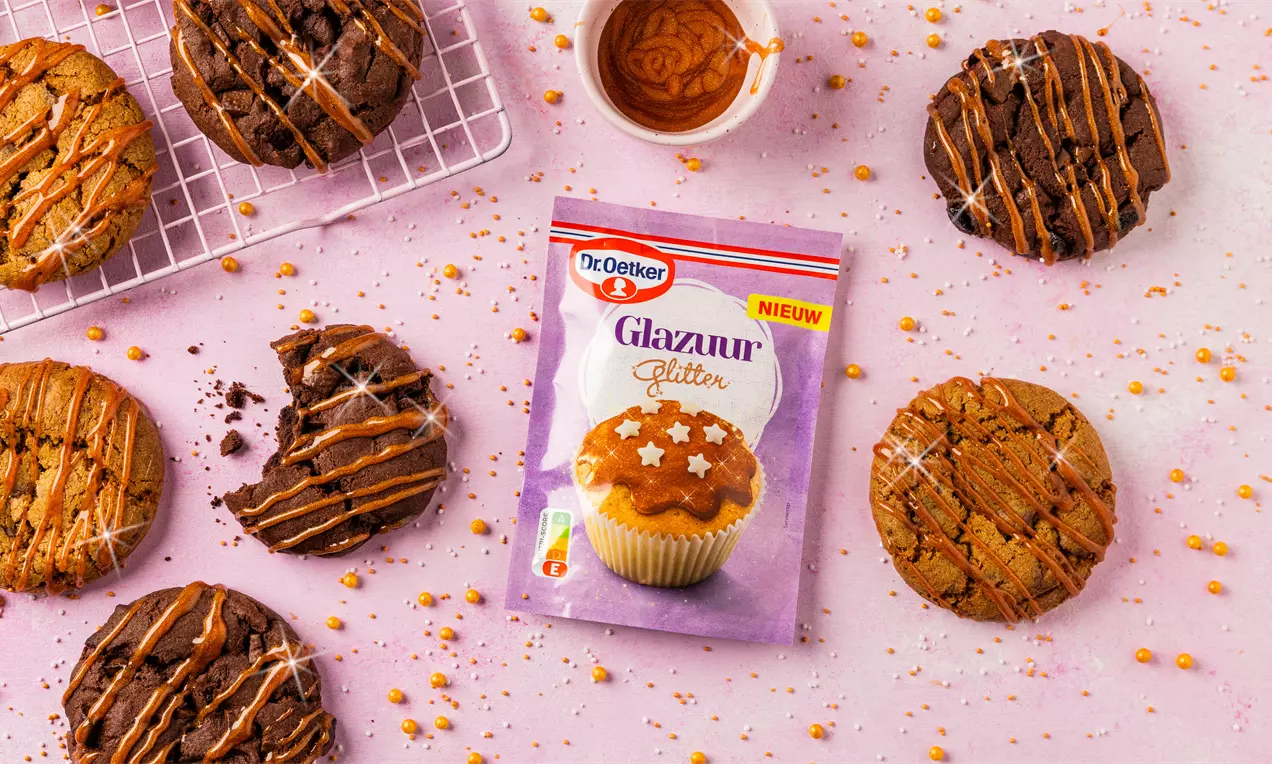Ronde chocolade- en vanillekoekjes, gedecoreerd met glanzende karameldrizzle en sprankelende glitter, op een roze ondergrond met topping-accenten
