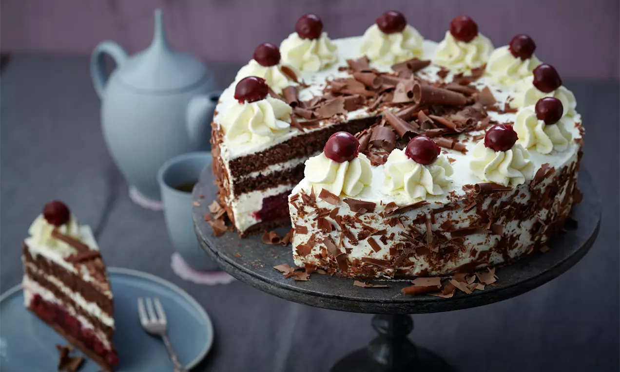 Schwarzwälder Kirschtorte met lagen donkere chocoladecake, slagroom, chocoladekrullen en kersen op een zwart serveerplateau
