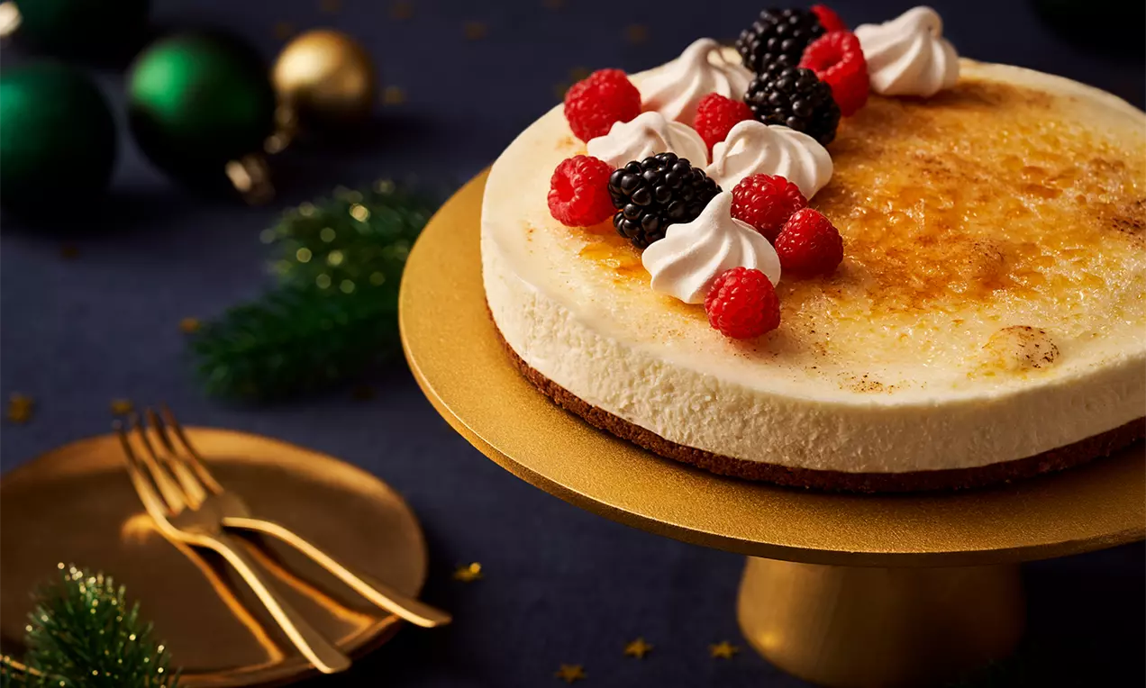 Ronde crème brûlée taart met een goudbruine gekarameliseerde bovenkant, gegarneerd met slagroom, frambozen en bramen op een gouden taartschaal